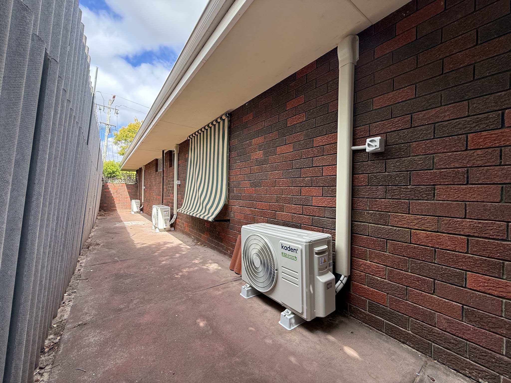 Three Kaden outdoor units installed down the side path of a brick house