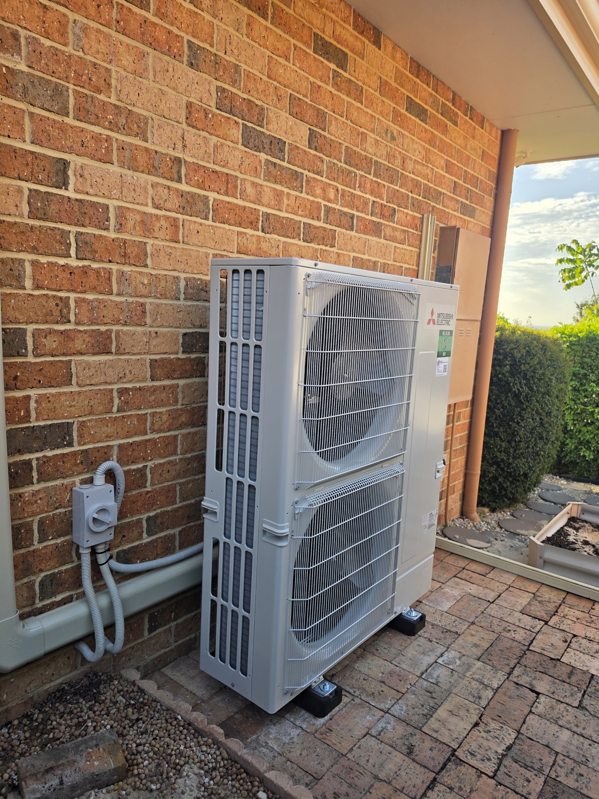 A large Mitsubishi Electric outdoor unit on a paved patio at sunset